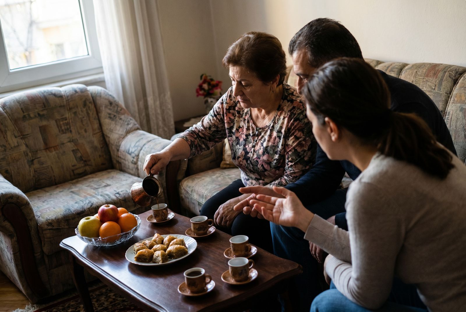 Gedeckter Tisch mit Kaffee und Gebäck in einem albanischen Wohnzimmer, mehrere Menschen sitzen beisammen