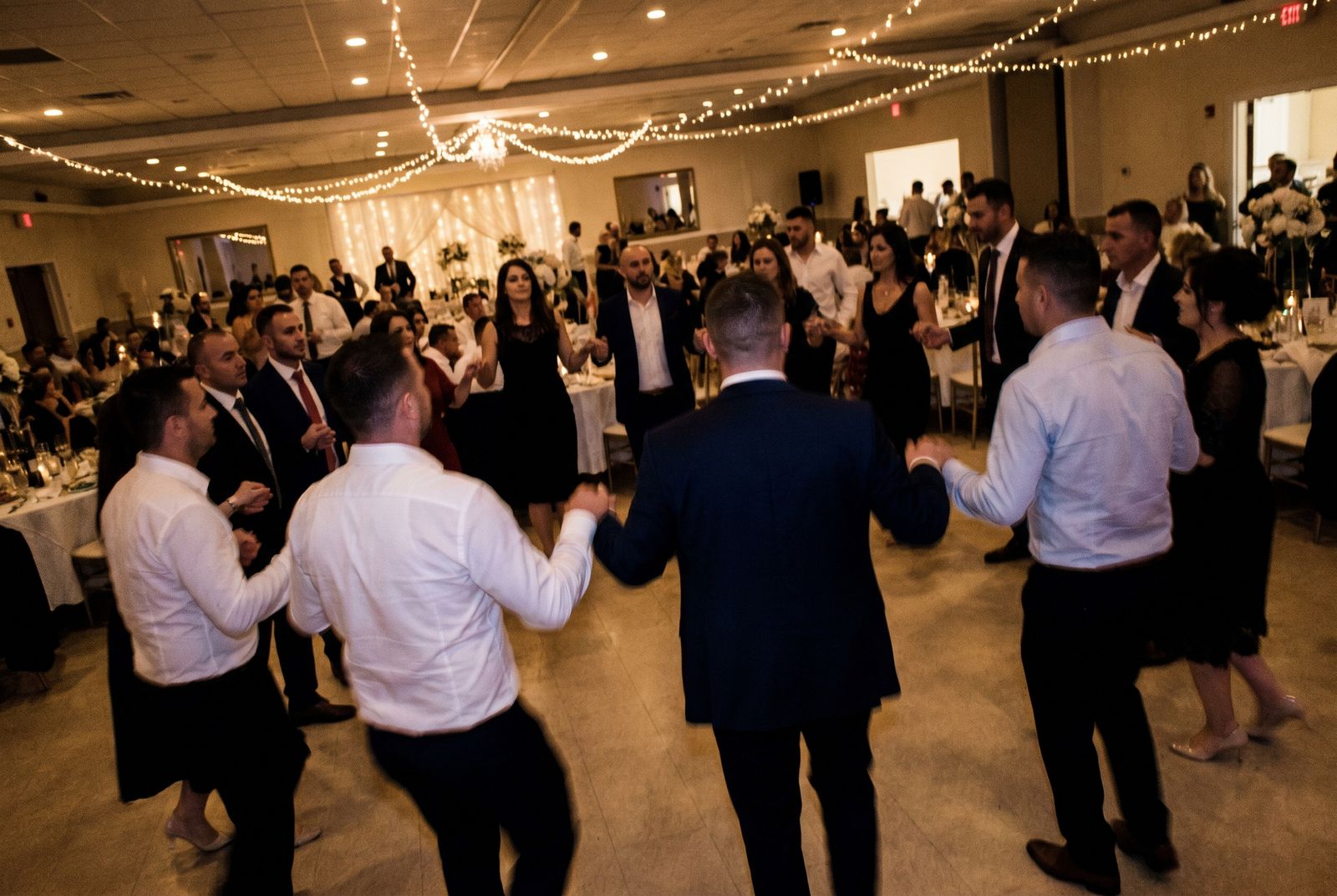 Gäste tanzen im Kreis auf einer albanischen Hochzeit in einem geschmückten Festsaal