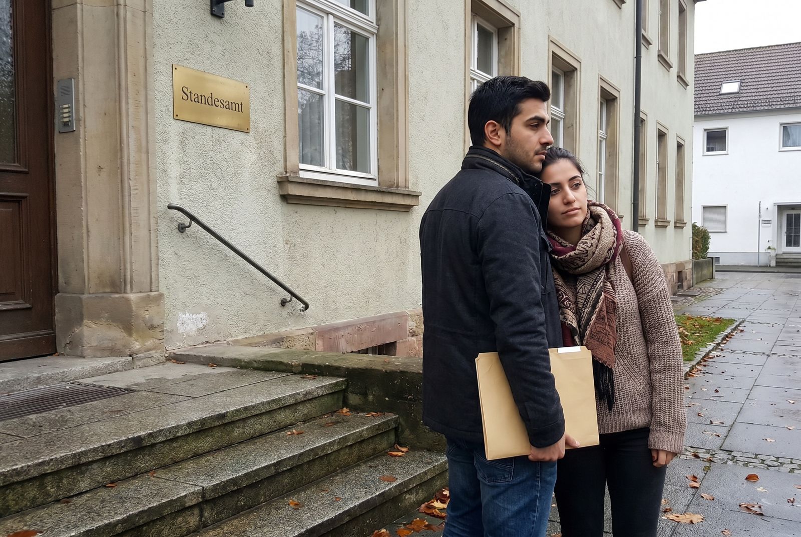Junges Paar mit Dokumentenmappe vor einem Standesamt in Deutschland, beiläufiger Moment