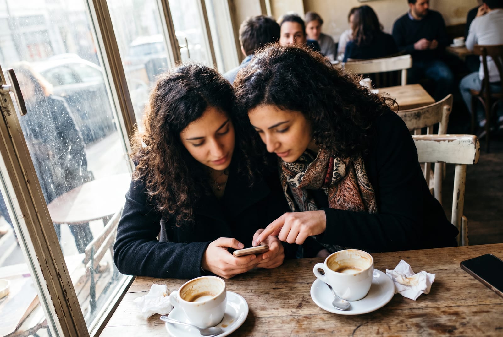 Zwei Freundinnen sitzen im Café und vergleichen Dating-Apps auf ihren Handys