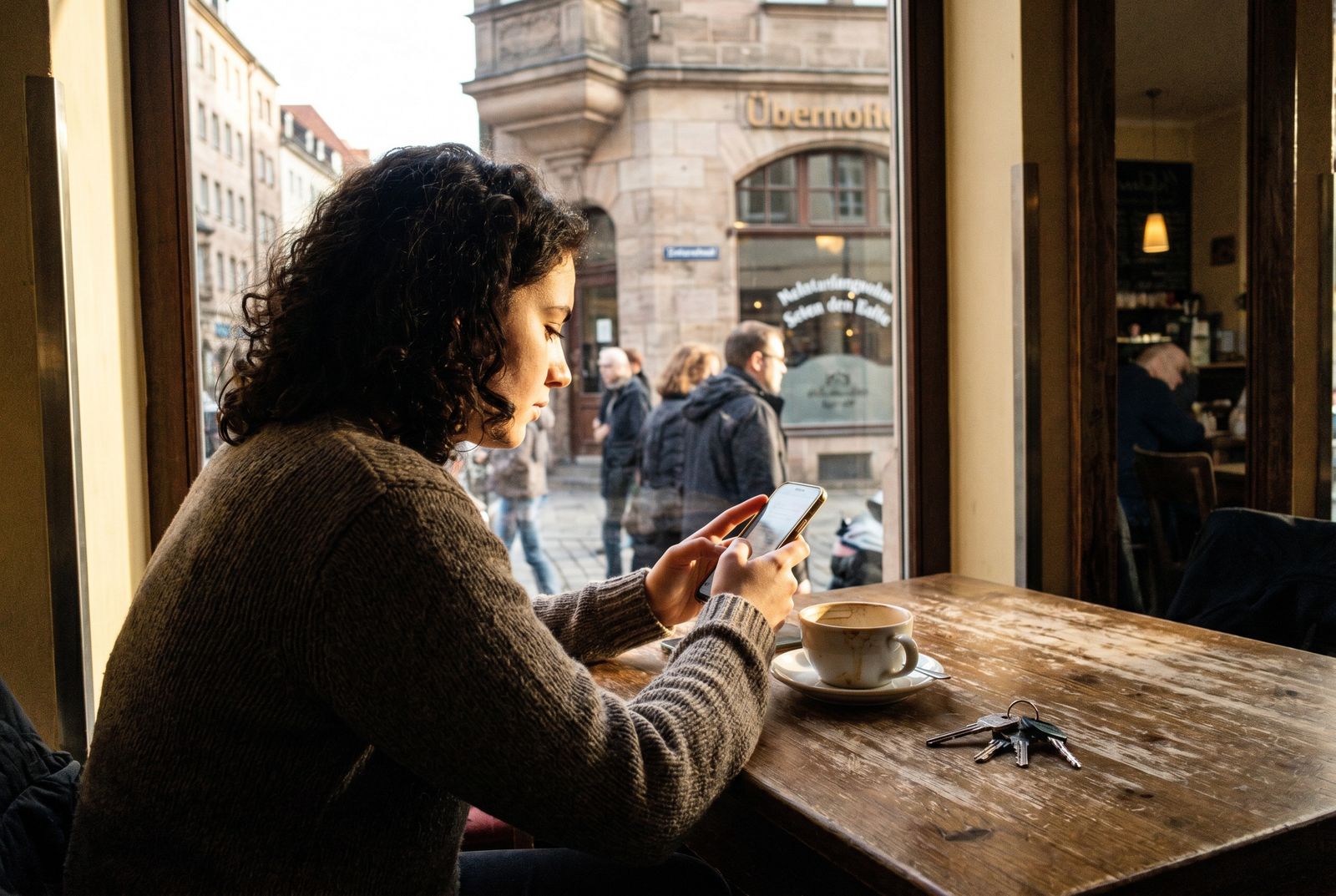 Junge Person sitzt in einem Café und tippt am Smartphone eine Nachricht